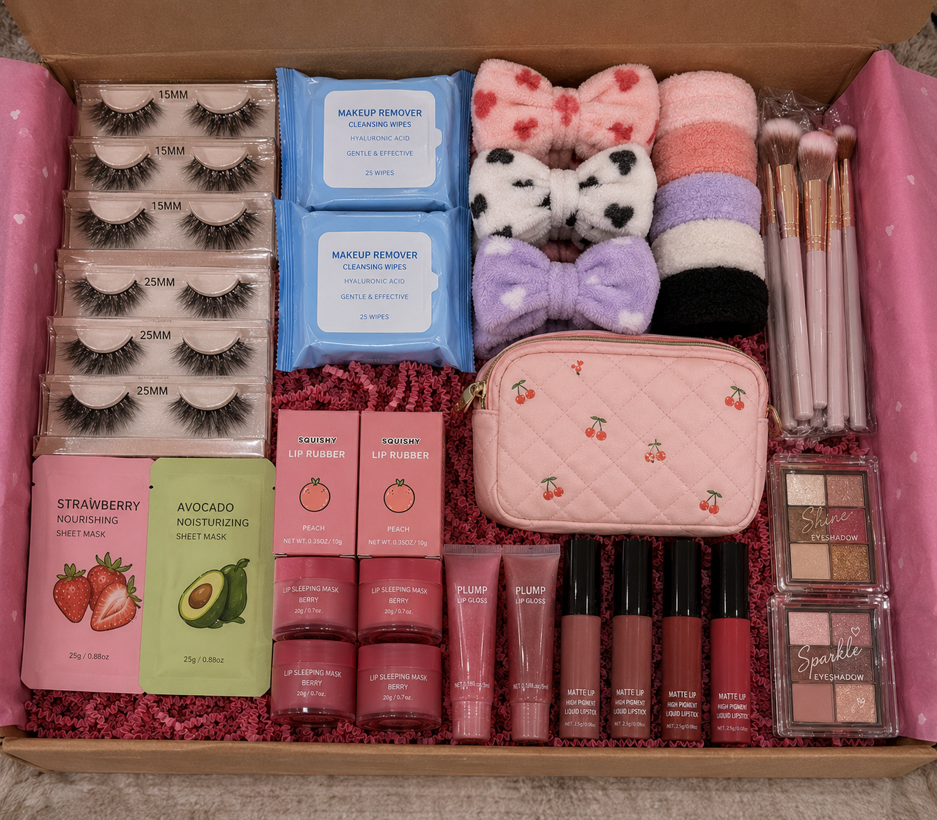 Assorted cosmetic items including makeup remover wipes, lip products, and a pink pouch in a box.