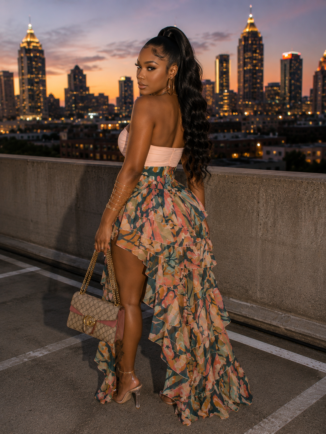Woman in a floral dress standing on a rooftop with a city skyline at sunset.
